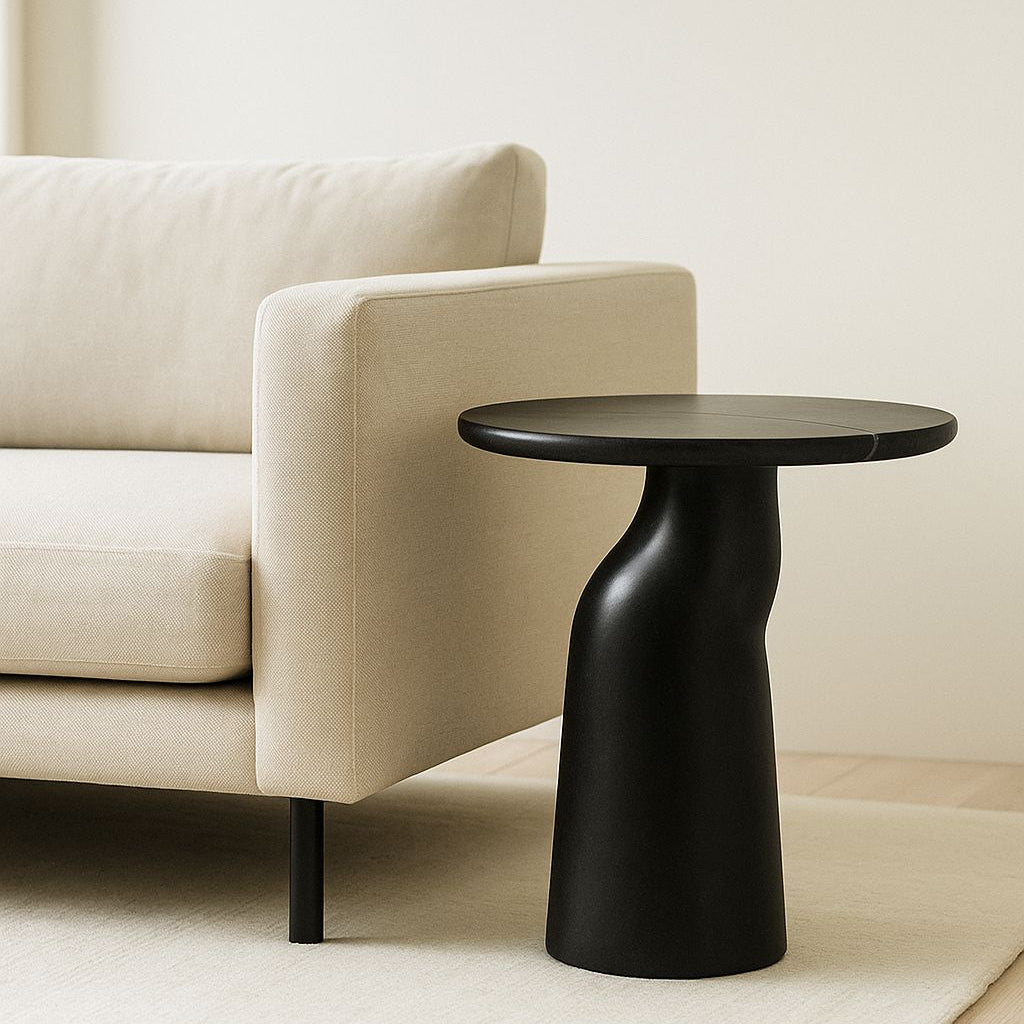 Black side table next to a beige sofa in a minimalistic room.