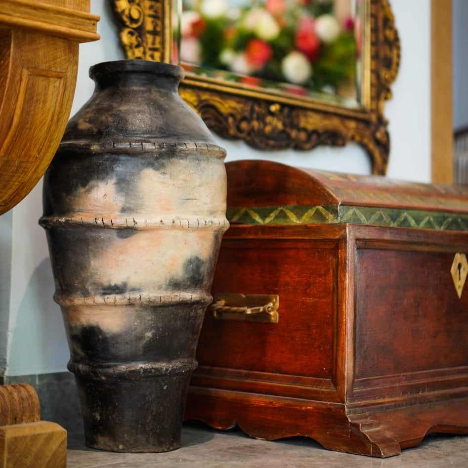 Vintage urn and wooden chest with decorative mirror in the background