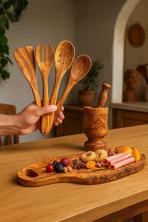 Olive wooden utensils held by a hand on a wooden table with food items.