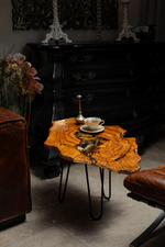 AI-styled view of Zitun Atelier table 003, an olive wood resin side table with black resin dried flowers, in a dark interior beside leather seating.