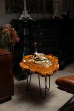 AI-styled view of Zitun Atelier table 007, an olive wood resin side table with white resin dried flowers, in a dark interior beside leather seating.