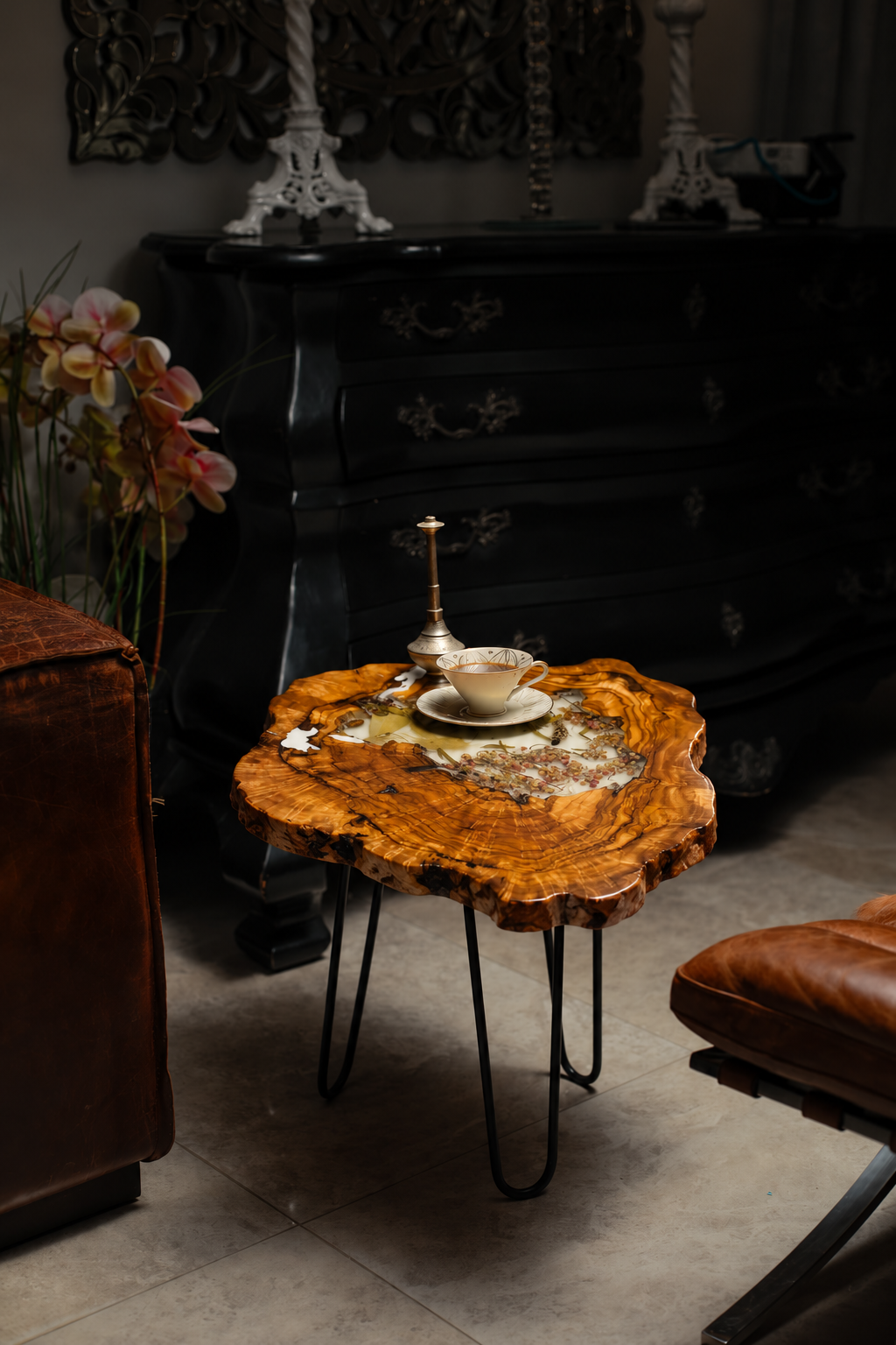 AI-styled view of Zitun Atelier table 007, an olive wood resin side table with white resin dried flowers, in a dark interior beside leather seating.
