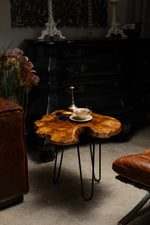 AI-styled view of Zitun Atelier table 008, an olive wood resin side table with dark teal resin burl, in a dark interior beside leather seating.