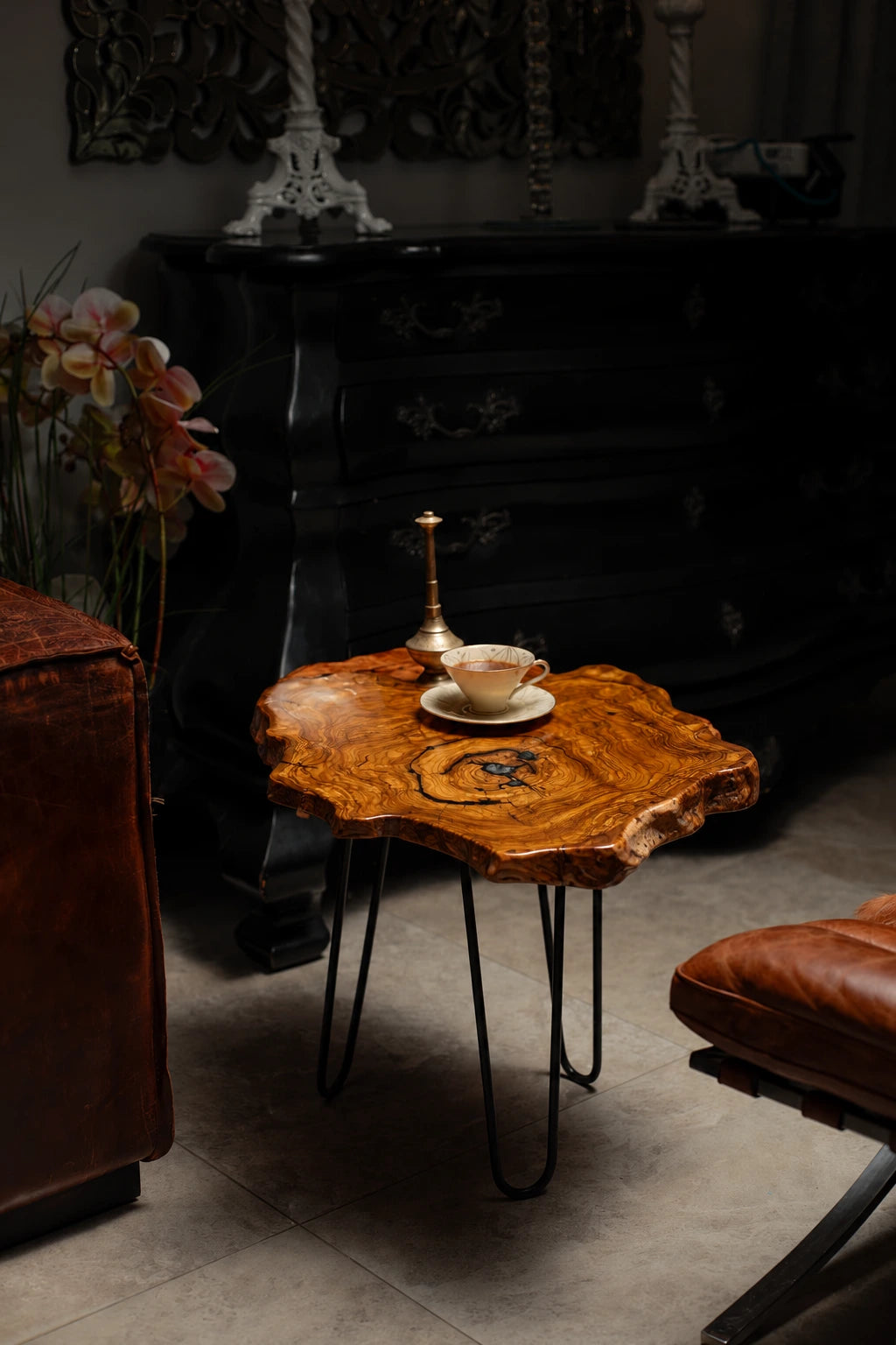 AI-styled view of Zitun Atelier table 010, an olive wood resin side table with black resin ring, in a dark interior beside leather seating.