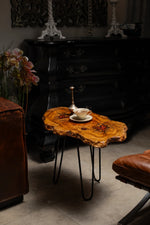 AI-styled view of Zitun Atelier table 011, an olive wood resin side table with red resin accents, in a dark interior beside leather seating.
