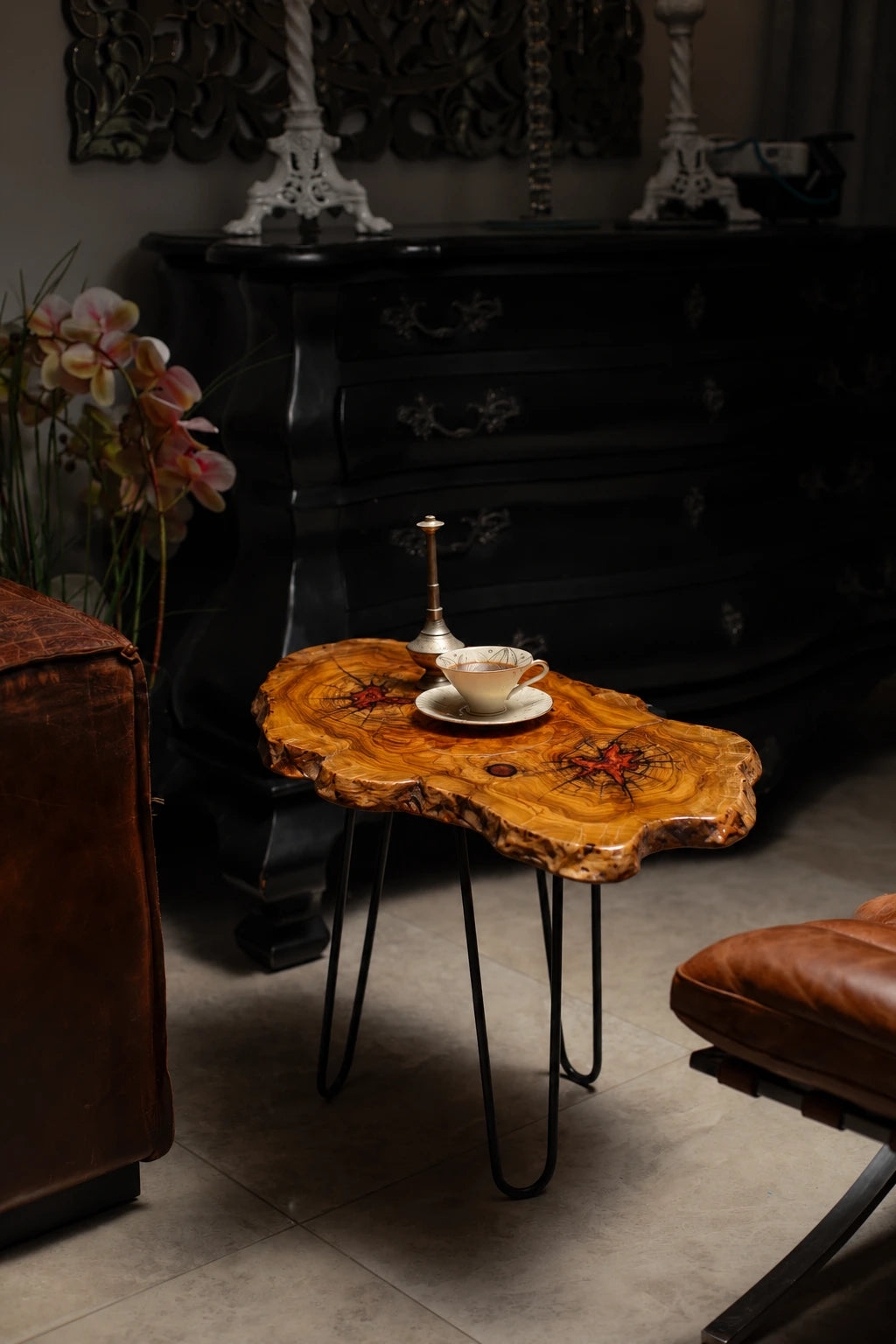 AI-styled view of Zitun Atelier table 011, an olive wood resin side table with red resin accents, in a dark interior beside leather seating.