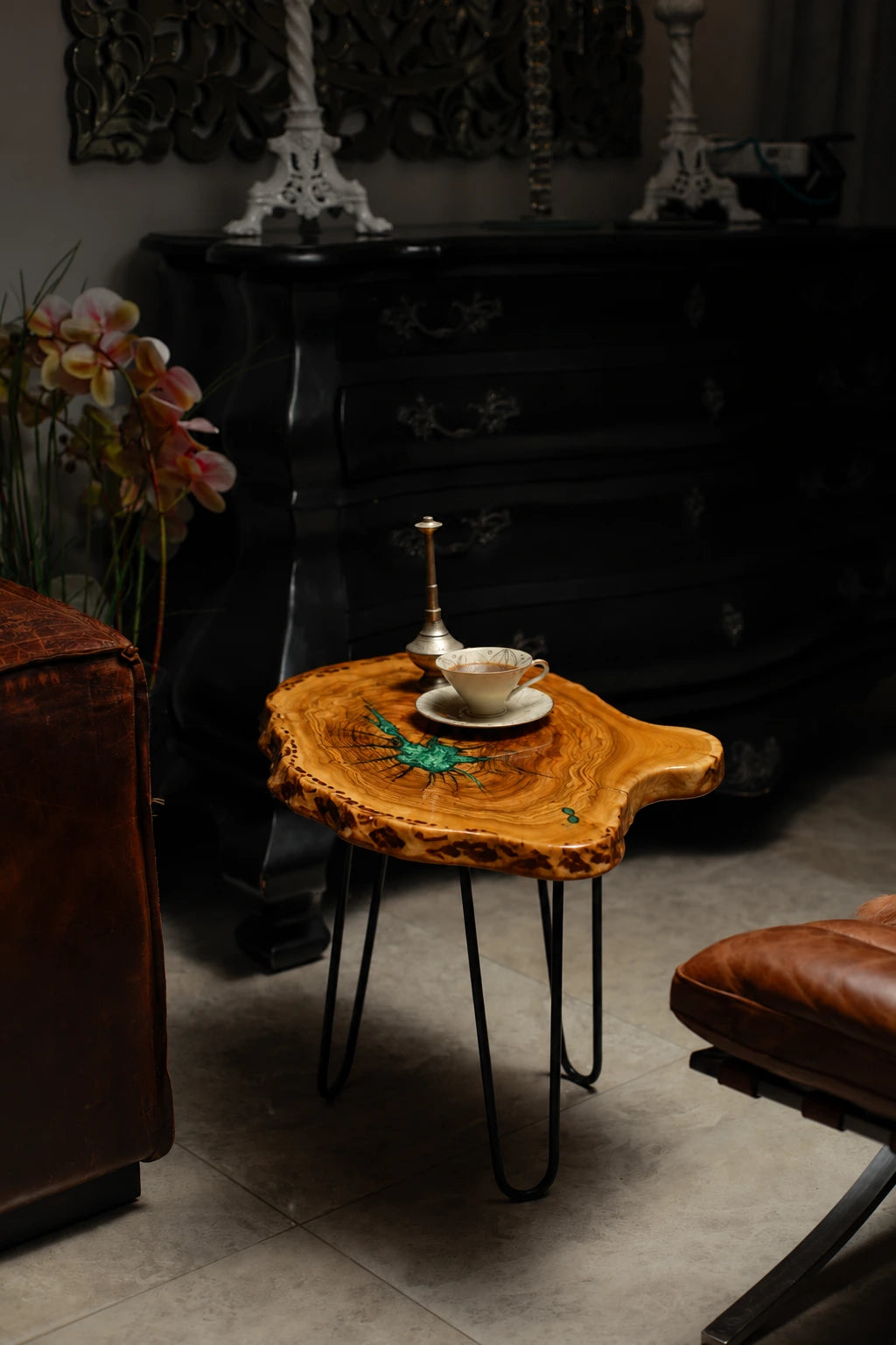 AI-styled view of Zitun Atelier table 012, an olive wood resin side table with emerald green star resin, in a dark interior beside leather seating.