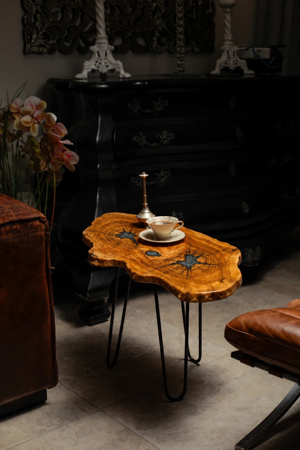 AI-styled view of Zitun Atelier table 013, an olive wood resin side table with teal starburst resin, in a dark interior beside leather seating.