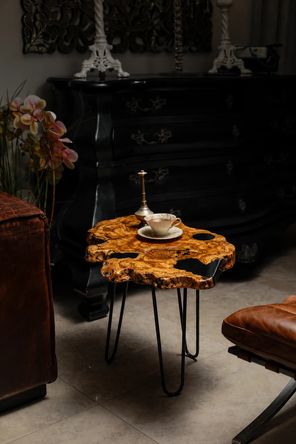 AI-styled view of Zitun Atelier table 014, an olive wood resin side table with black resin holes, in a dark interior beside leather seating.