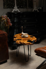AI-styled view of Zitun Atelier table 014, an olive wood resin side table with black resin holes, in a dark interior beside leather seating.