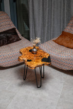 AI-styled view of Zitun Atelier table 014, an olive wood resin side table with black resin holes, viewed from above between two upholstered armchairs.