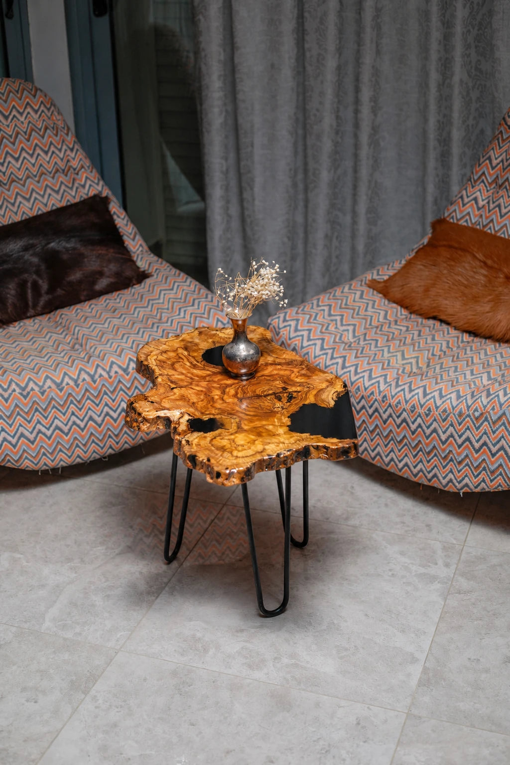AI-styled view of Zitun Atelier table 014, an olive wood resin side table with black resin holes, viewed from above between two upholstered armchairs.