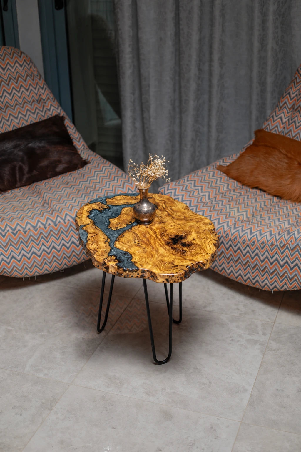 AI-styled view of Zitun Atelier table 015, an olive wood resin side table with blue grey resin river, viewed from above between two upholstered armchairs.