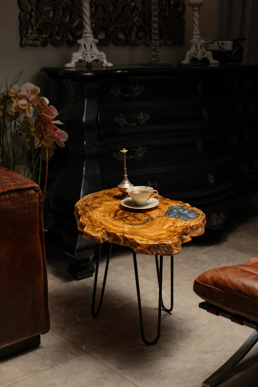 AI-styled view of Zitun Atelier table 016, an olive wood resin side table with grey resin inlay, in a dark interior beside leather seating.