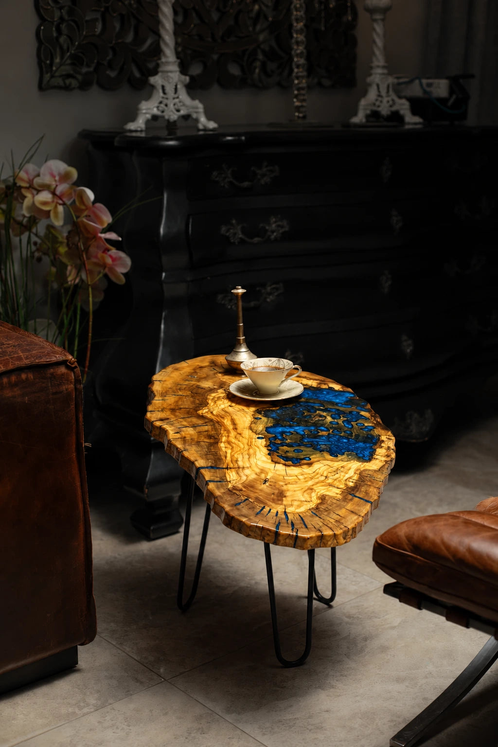 AI-styled view of Zitun Atelier table 017, an olive wood resin small coffee table with blue resin pool, in a dark interior beside leather seating.