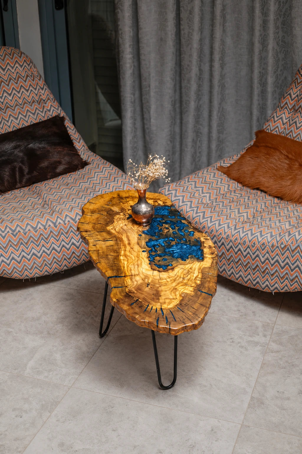 AI-styled view of Zitun Atelier table 017, an olive wood resin small coffee table with blue resin pool, viewed from above between two upholstered armchairs.
