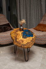 AI-styled view of Zitun Atelier table 017, an olive wood resin small coffee table with blue resin pool, in a lounge setting with a vase on the tabletop.