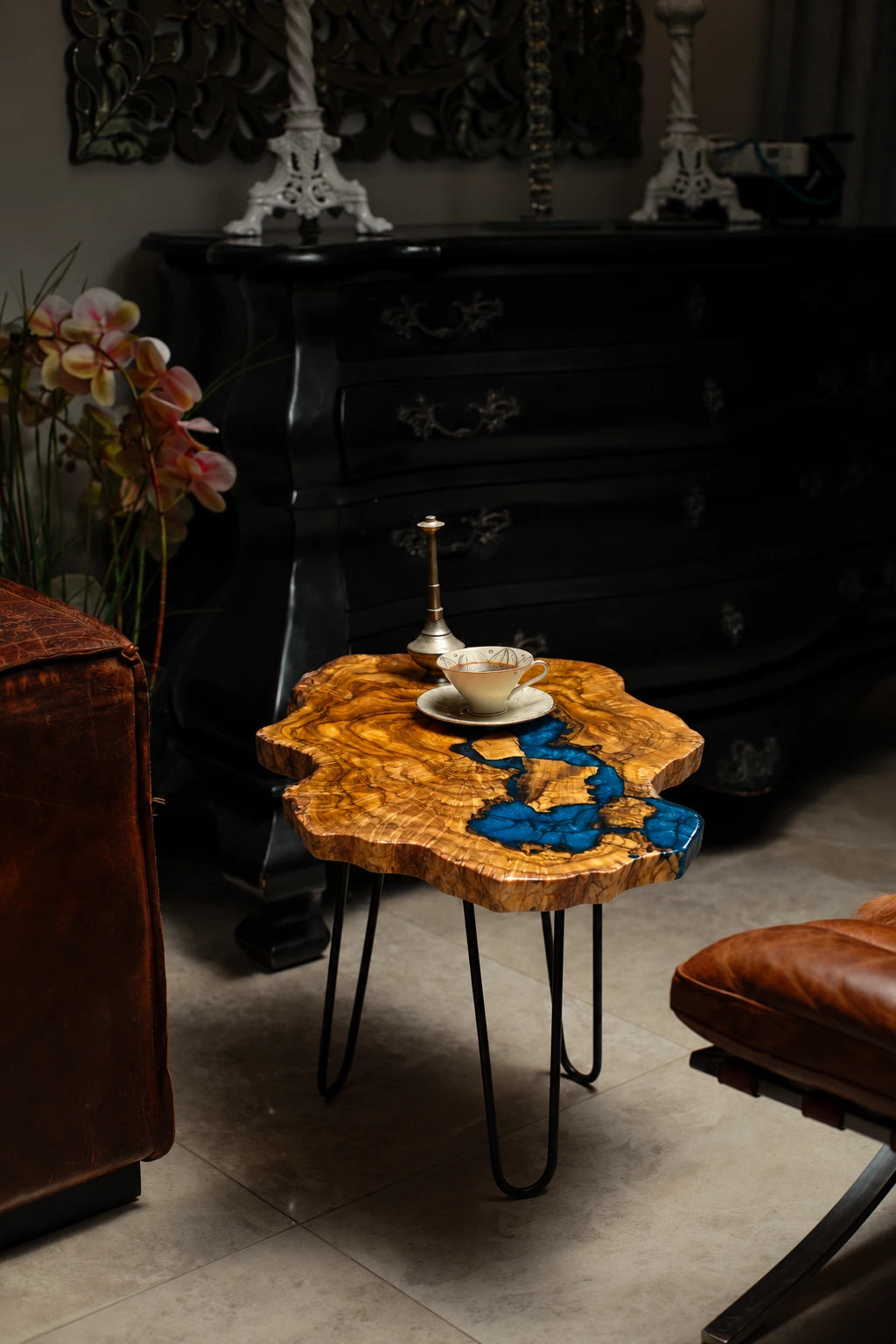 AI-styled view of Zitun Atelier table 020, an olive wood resin side table with electric blue resin river, in a dark interior beside leather seating.