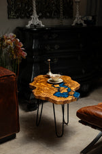 AI-styled view of Zitun Atelier table 020, an olive wood resin side table with electric blue resin river, in a dark interior beside leather seating.