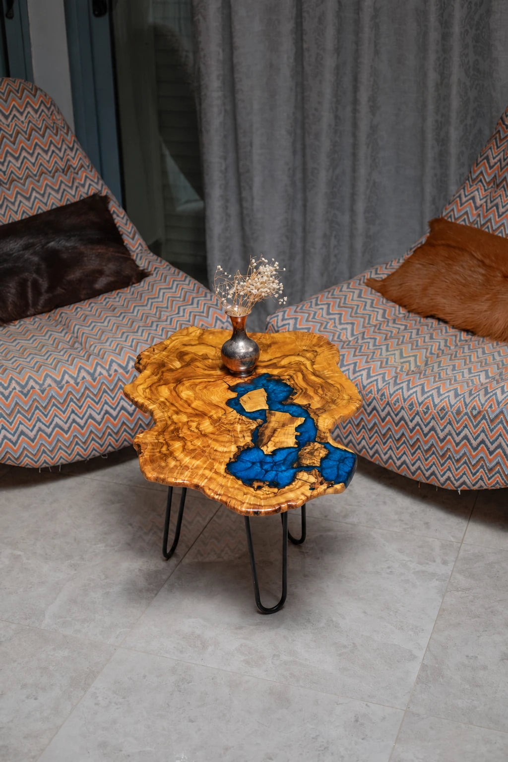 AI-styled view of Zitun Atelier table 020, an olive wood resin side table with electric blue resin river, viewed from above between two upholstered armchairs.