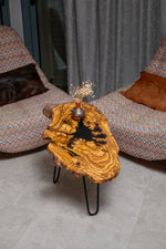 AI-styled view of Zitun Atelier table 021, an olive wood resin side table with black resin splash, viewed from above between two upholstered armchairs.