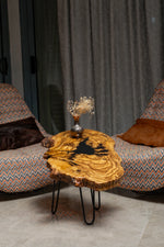 AI-styled view of Zitun Atelier table 021, an olive wood resin side table with black resin splash, in a lounge setting with a vase on the tabletop.