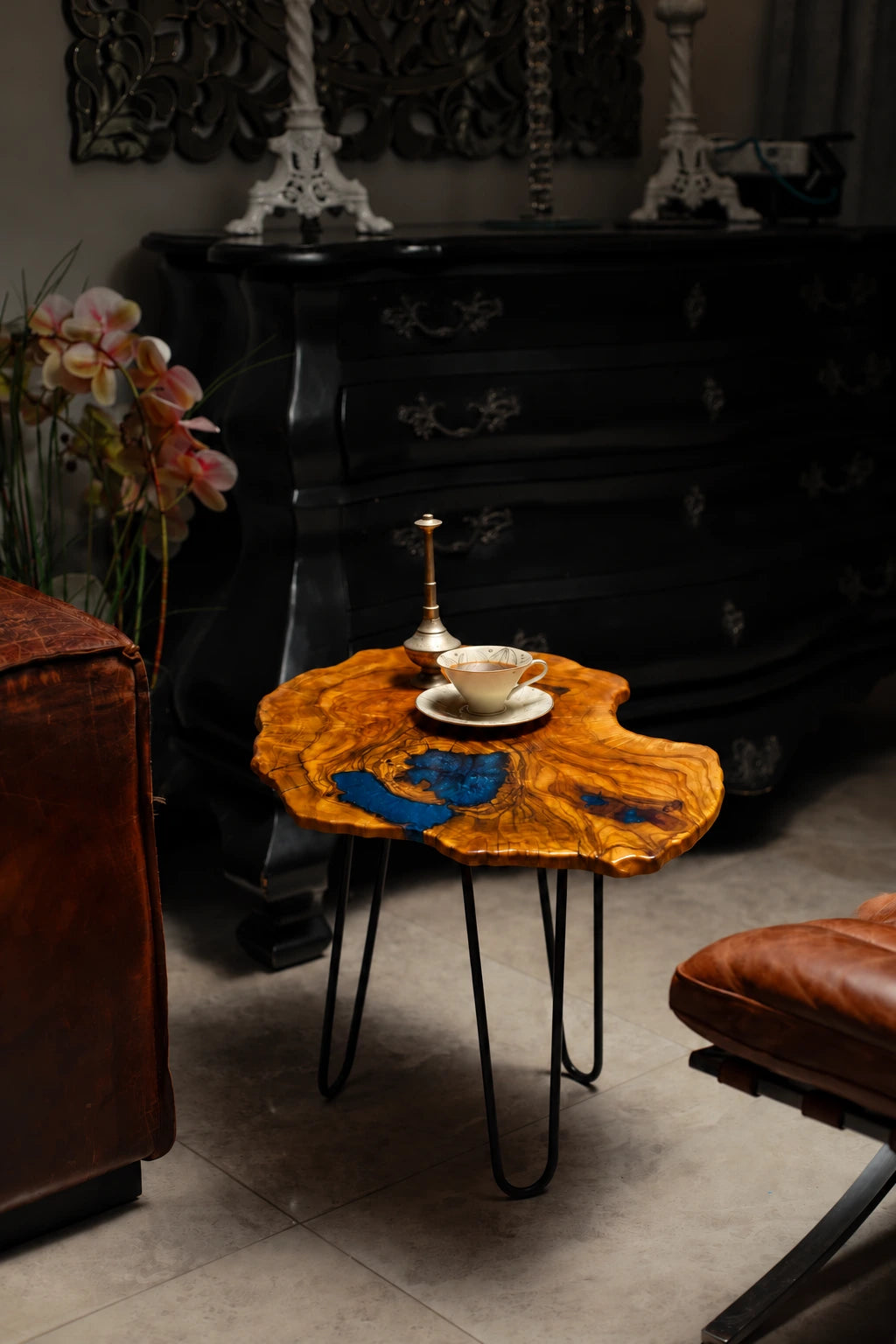 AI-styled view of Zitun Atelier table 022, an olive wood resin side table with blue resin inlay, in a dark interior beside leather seating.