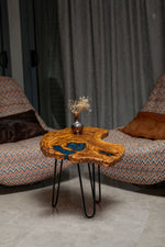 AI-styled view of Zitun Atelier table 022, an olive wood resin side table with blue resin inlay, in a lounge setting with a vase on the tabletop.