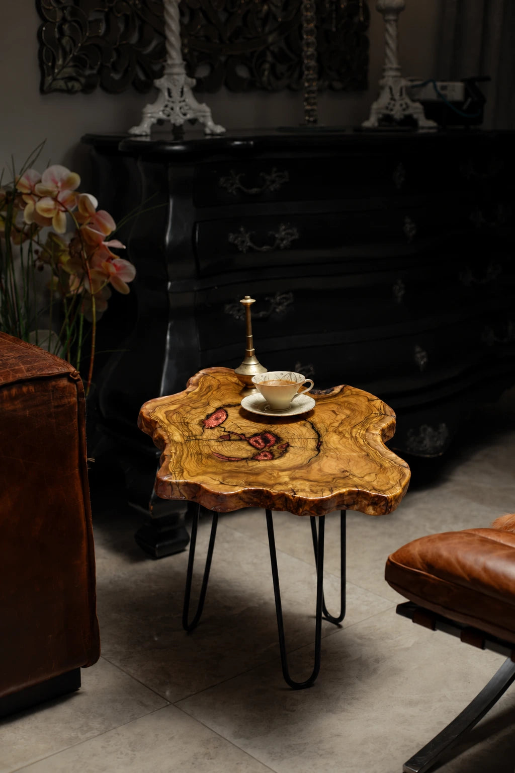 AI-styled view of Zitun Atelier table 023, an olive wood resin side table with copper red resin inlay, in a dark interior beside leather seating.