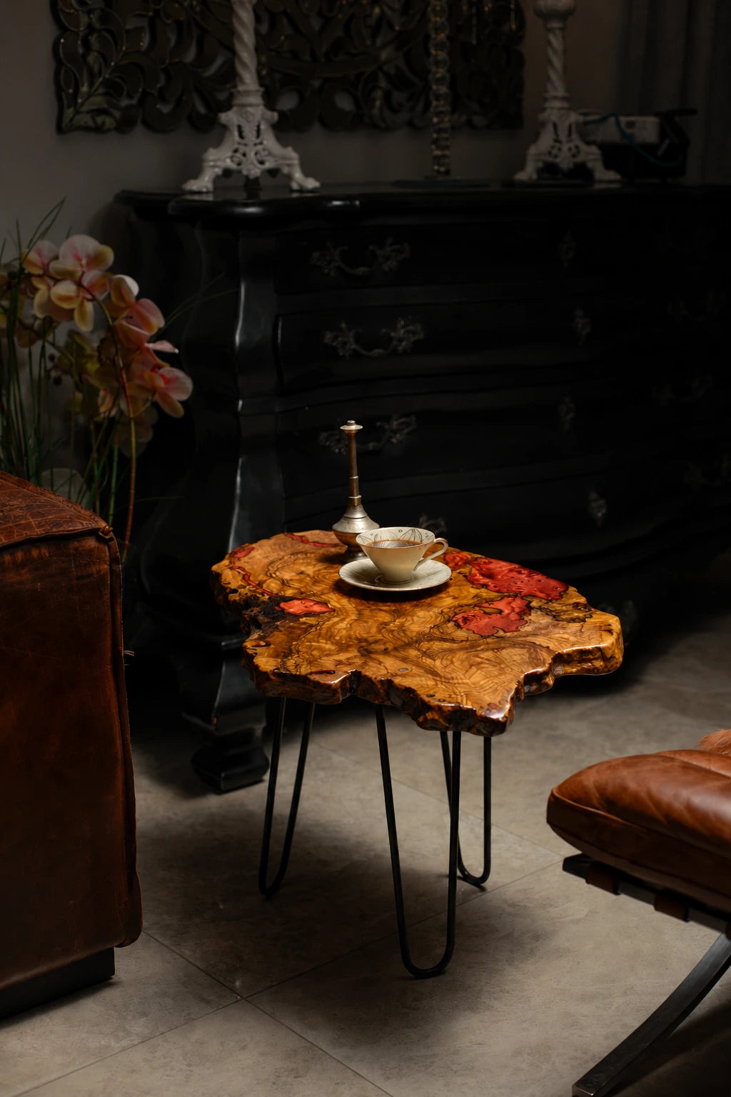 AI-styled view of Zitun Atelier table 023, an olive wood resin side table with copper red resin inlay, in a dark interior beside leather seating.