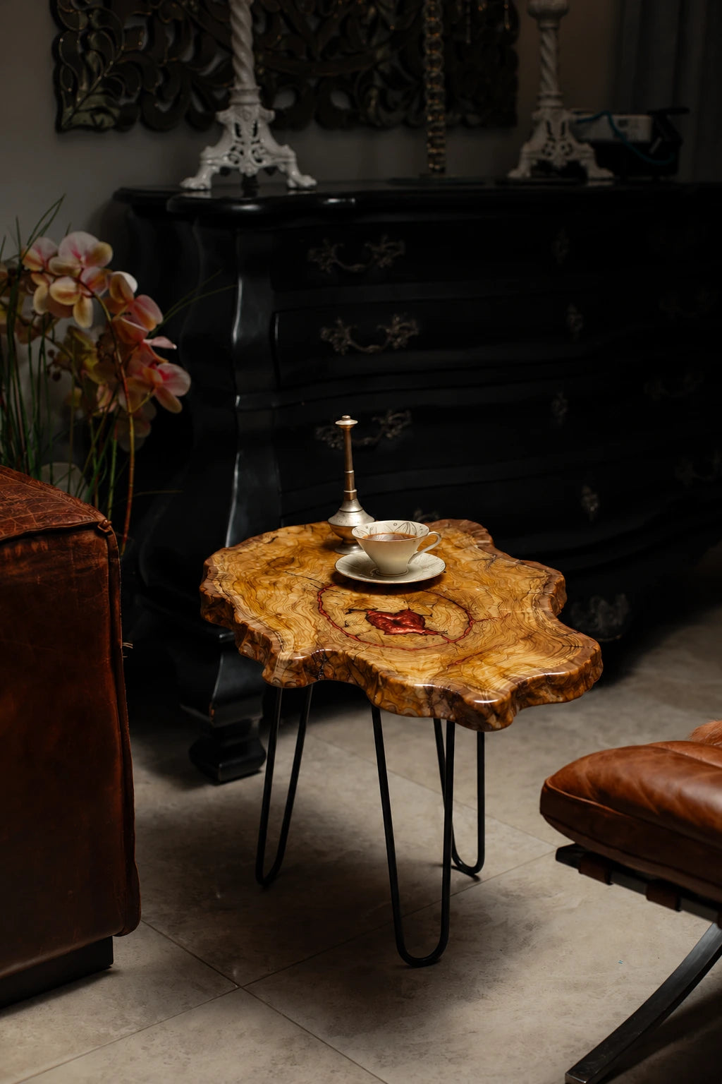 AI-styled view of Zitun Atelier table 024, an olive wood resin side table with copper red resin center, in a dark interior beside leather seating.
