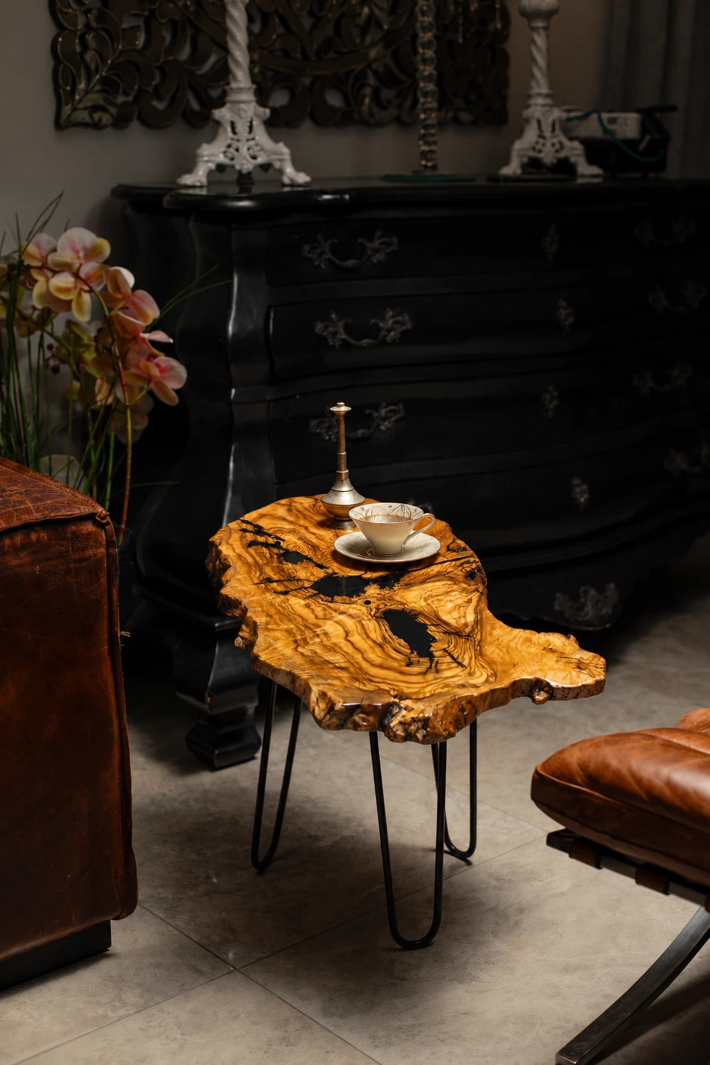 AI-styled view of Zitun Atelier table 026, an olive wood resin side table with black resin veins, in a dark interior beside leather seating.
