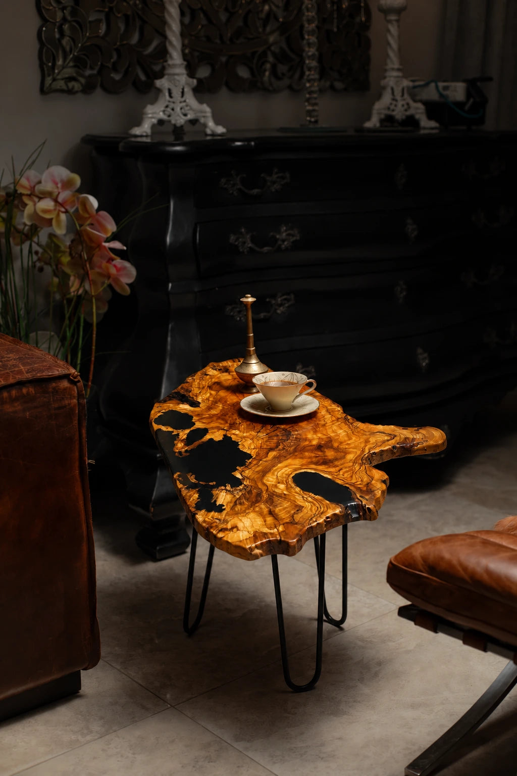 AI-styled view of Zitun Atelier table 027, an olive wood resin side table with black resin live edge, in a dark interior beside leather seating.