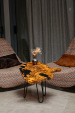 AI-styled view of Zitun Atelier table 027, an olive wood resin side table with black resin live edge, in a lounge setting with a vase on the tabletop.