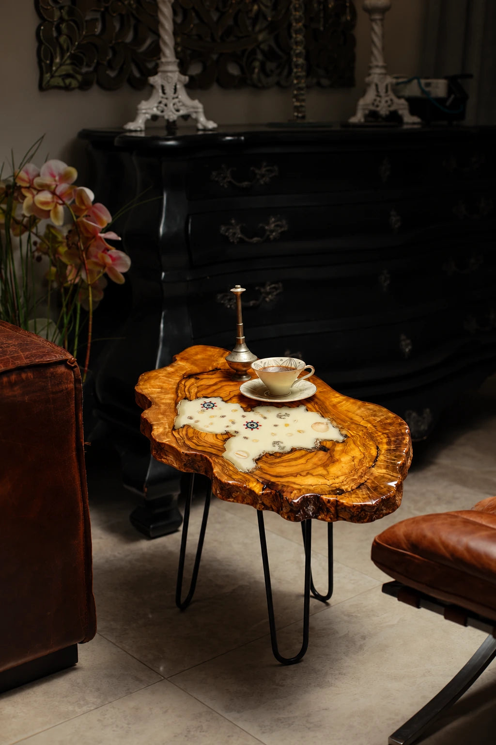 AI-styled view of Zitun Atelier table 028, an olive wood resin side table with white resin nautical charms, in a dark interior beside leather seating.