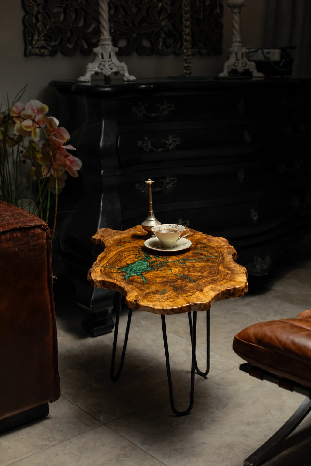 AI-styled view of Zitun Atelier table 031, an olive wood resin side table with emerald green resin veins, in a dark interior beside leather seating.