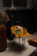 AI-styled view of Zitun Atelier table 033, an olive wood resin side table with green malachite resin, in a dark interior beside leather seating.