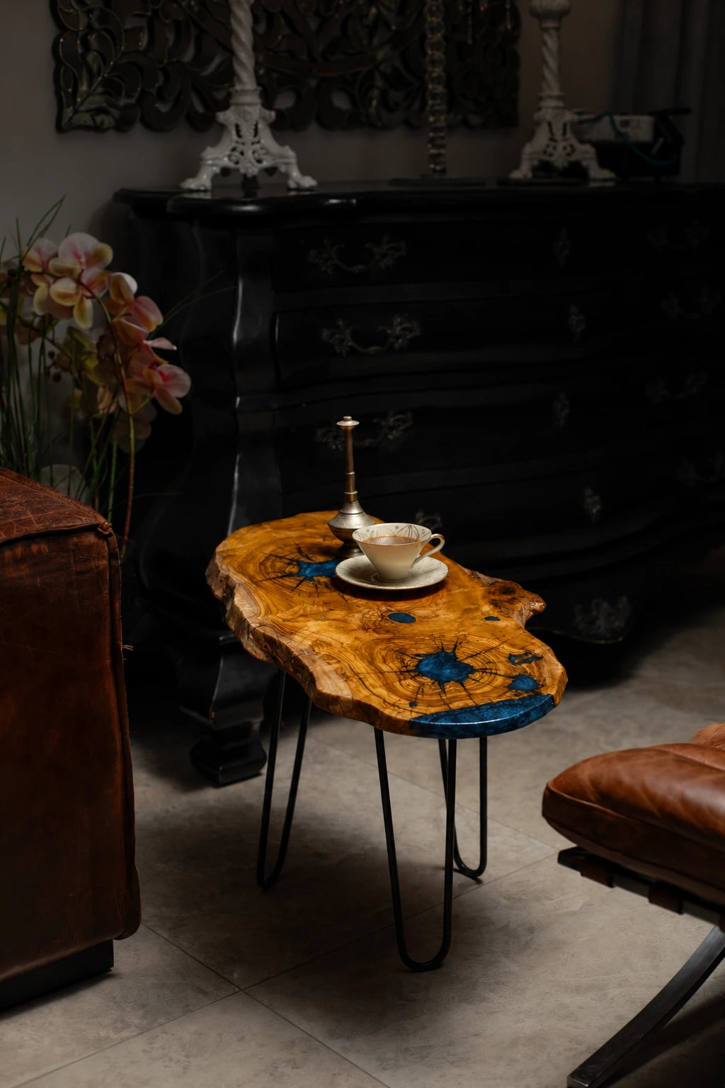 AI-styled view of Zitun Atelier table 036, an olive wood resin side table with blue starburst resin, in a dark interior beside leather seating.