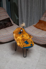 AI-styled view of Zitun Atelier table 036, an olive wood resin side table with blue starburst resin, viewed from above between two upholstered armchairs.