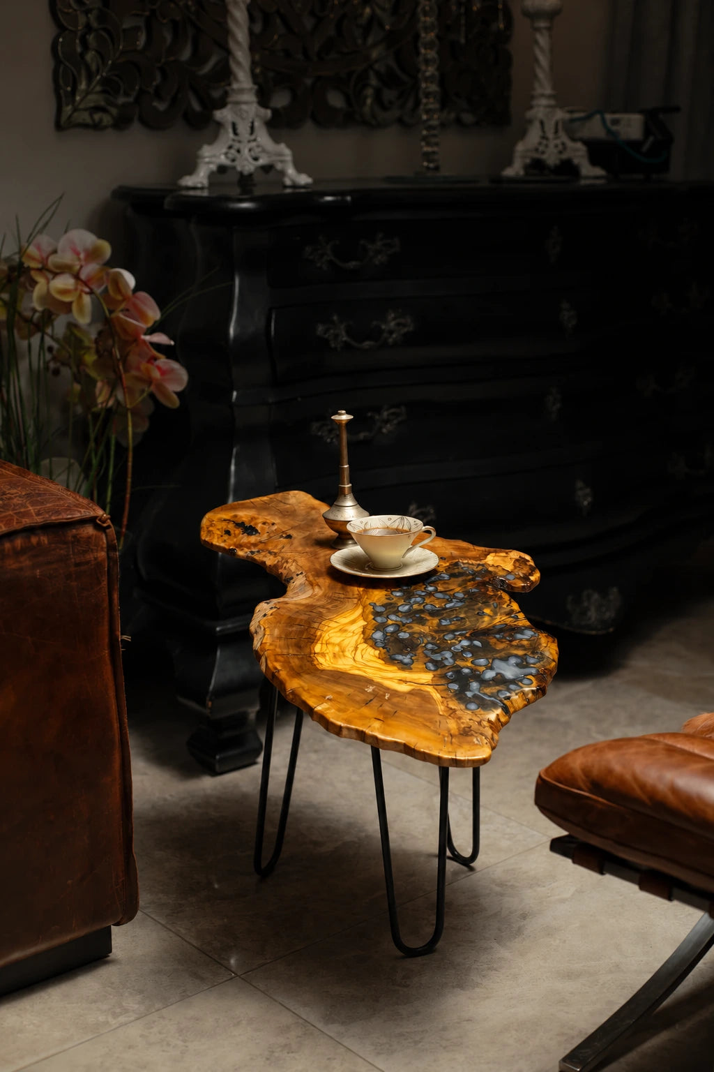 AI-styled view of Zitun Atelier table 037, an olive wood resin side table with blue pebble resin, in a dark interior beside leather seating.