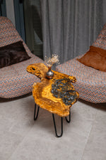 AI-styled view of Zitun Atelier table 037, an olive wood resin side table with blue pebble resin, viewed from above between two upholstered armchairs.
