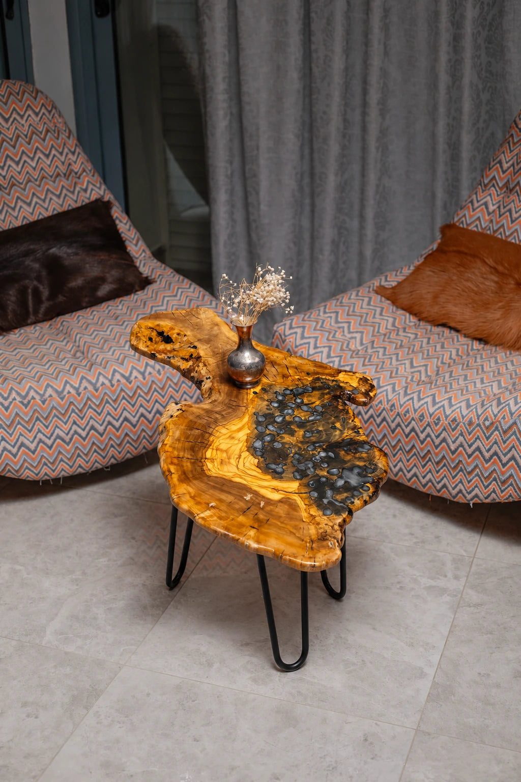 AI-styled view of Zitun Atelier table 037, an olive wood resin side table with blue pebble resin, viewed from above between two upholstered armchairs.