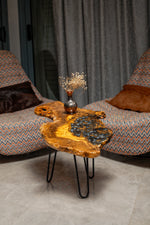 AI-styled view of Zitun Atelier table 037, an olive wood resin side table with blue pebble resin, in a lounge setting with a vase on the tabletop.
