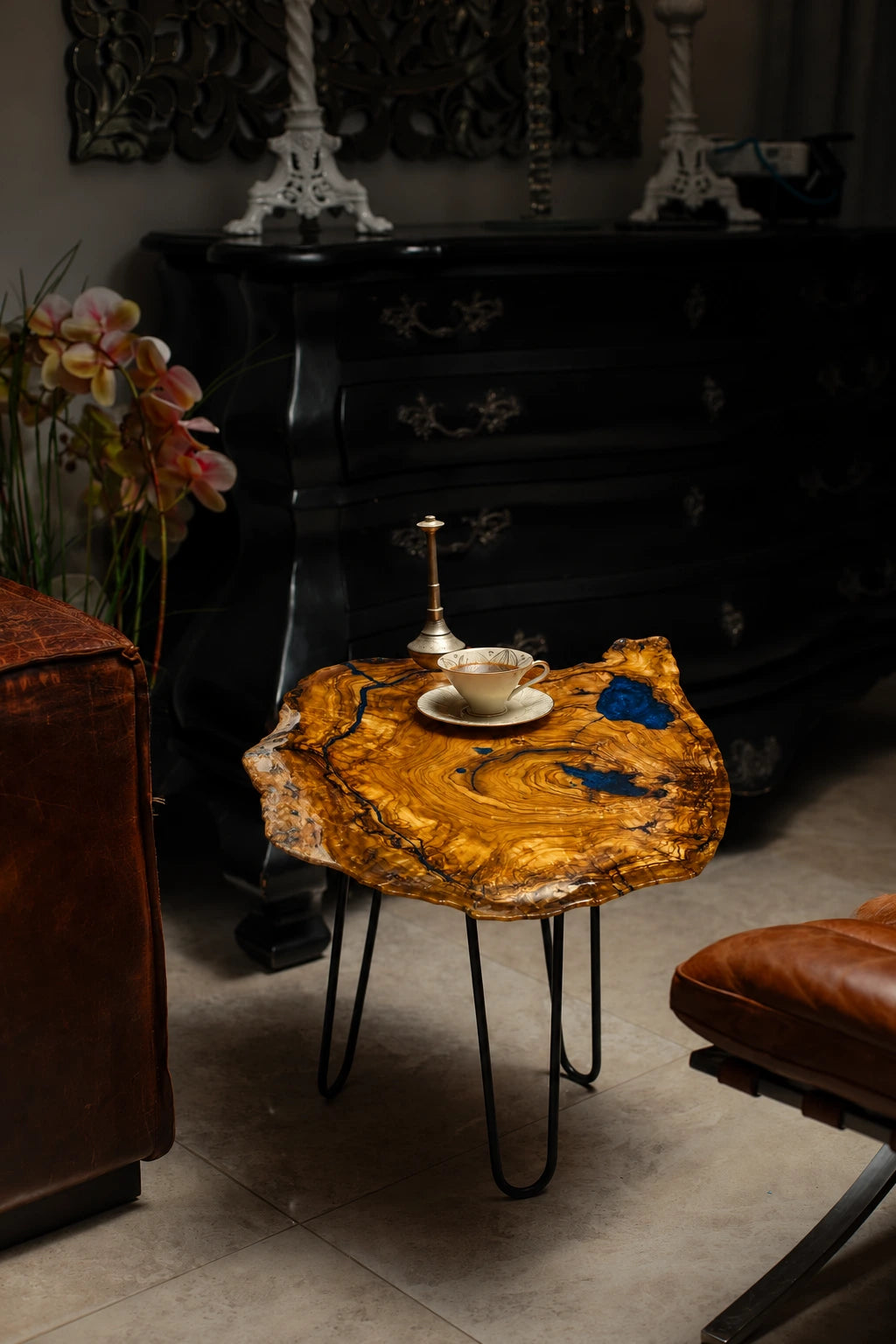 AI-styled view of Zitun Atelier table 038, an olive wood resin side table with blue resin accents, in a dark interior beside leather seating.