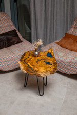AI-styled view of Zitun Atelier table 038, an olive wood resin side table with blue resin accents, viewed from above between two upholstered armchairs.