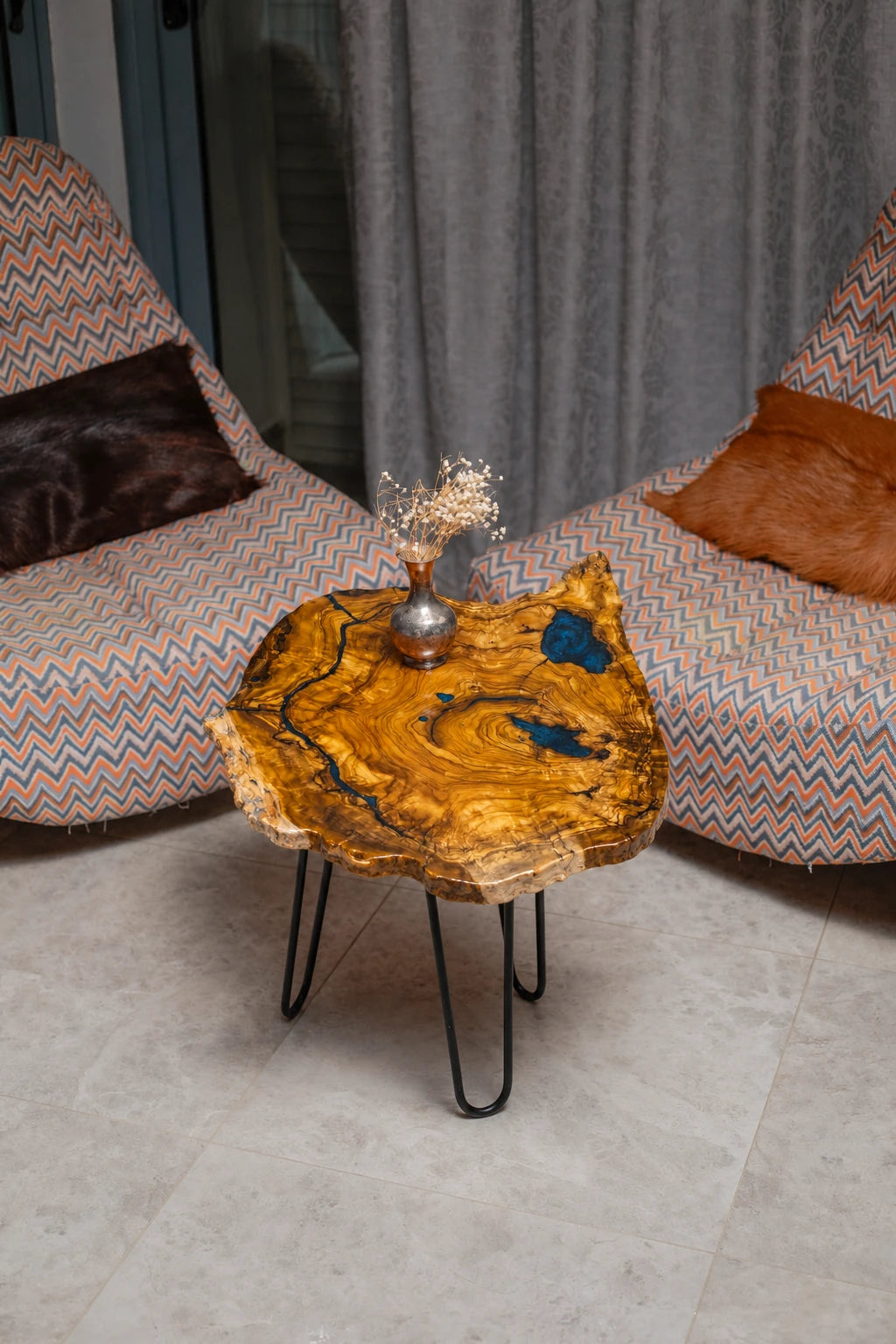 AI-styled view of Zitun Atelier table 038, an olive wood resin side table with blue resin accents, viewed from above between two upholstered armchairs.