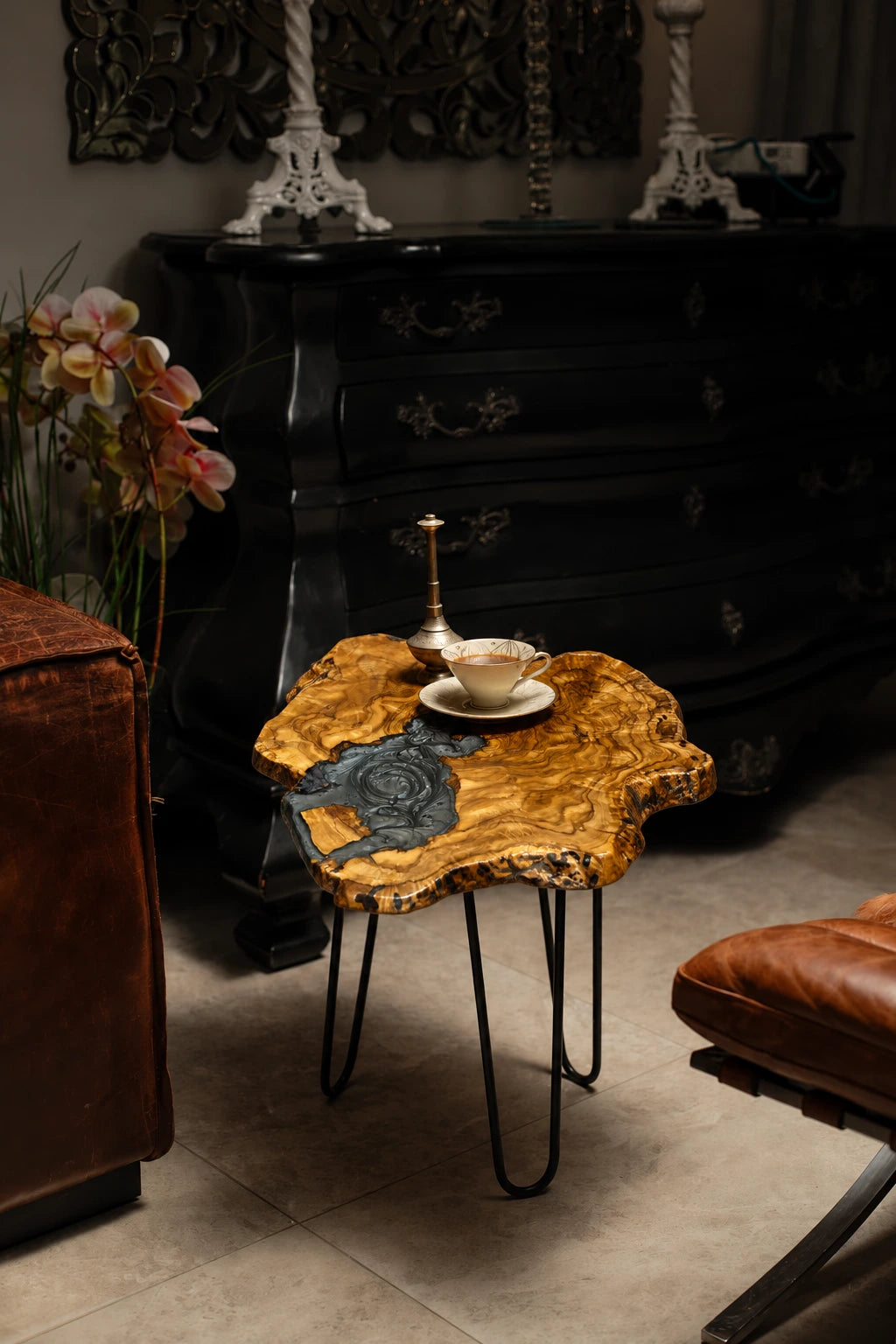 AI-styled view of Zitun Atelier table 039, an olive wood resin side table with grey swirl resin, in a dark interior beside leather seating.