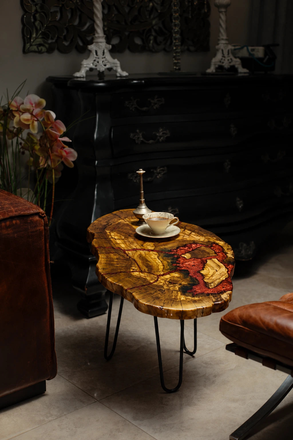 AI-styled view of Zitun Atelier table 042, an olive wood resin side table with red coral resin, in a dark interior beside leather seating.