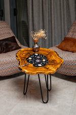 AI-styled view of Zitun Atelier table 044, an olive wood resin side table with black resin nautical charms, in a lounge setting with a vase on the tabletop.