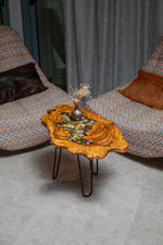AI-styled view of Zitun Atelier table 047, an olive wood resin side table with sea shell pebble resin, viewed from above between two upholstered armchairs.